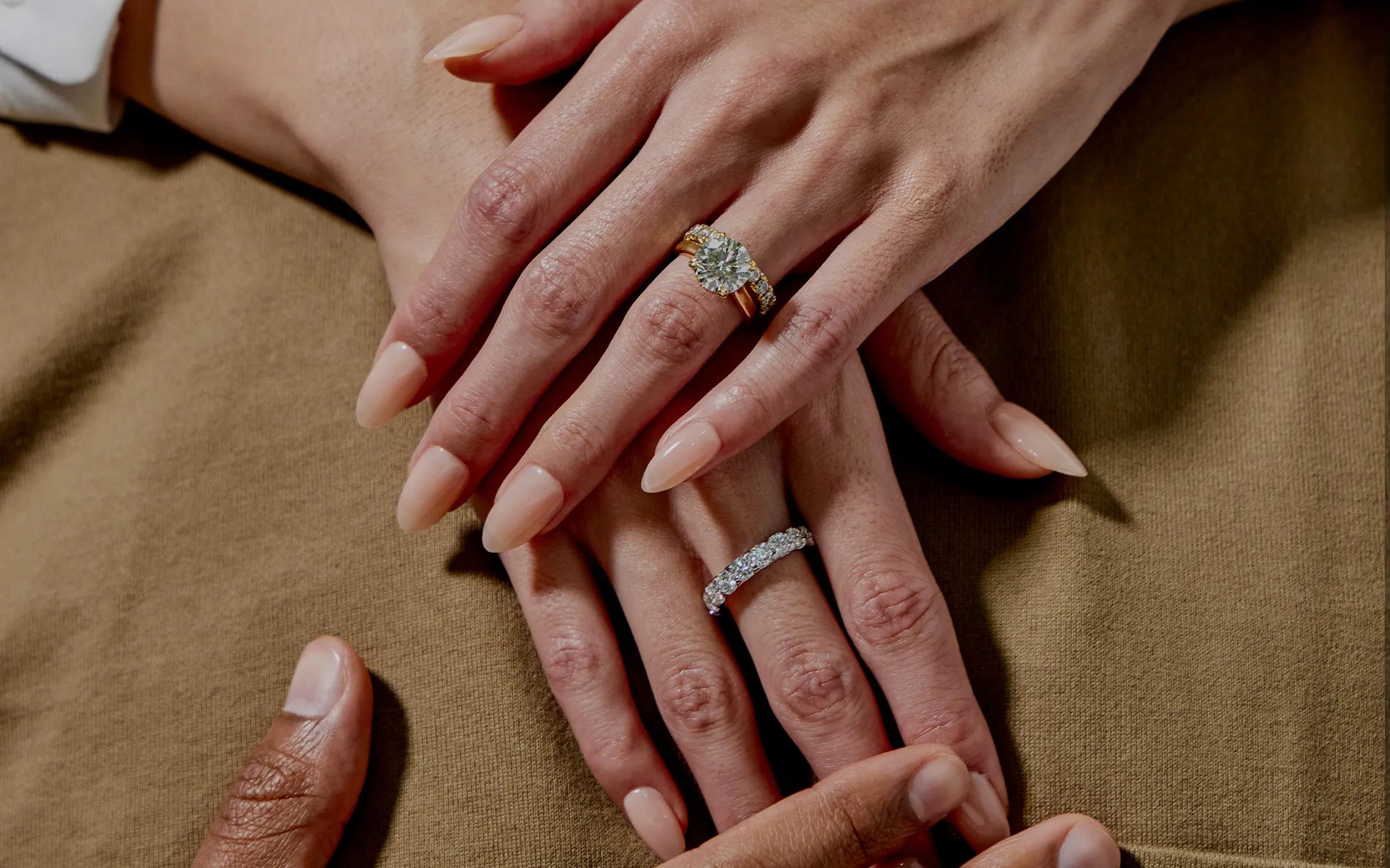 Two hands showing an engagement ring and a wedding band